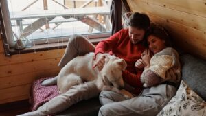 A couple enjoys a serene moment with their dog in a cozy wooden cabin.
